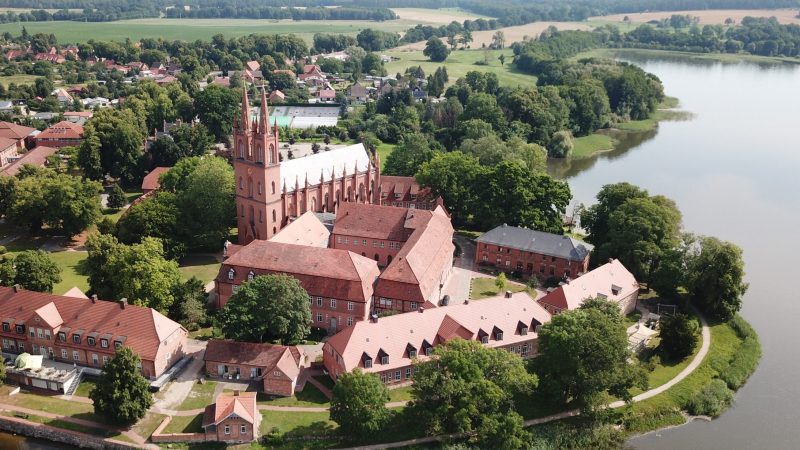 Luftaufnahme Klosterkirche Dobbertin mit zwei Kirchtürmen und weiteren Gebäuden am See